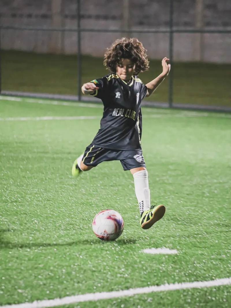 Atleta do Real Clube Aracaju, de uniforme preto, chuta a bola no gramado