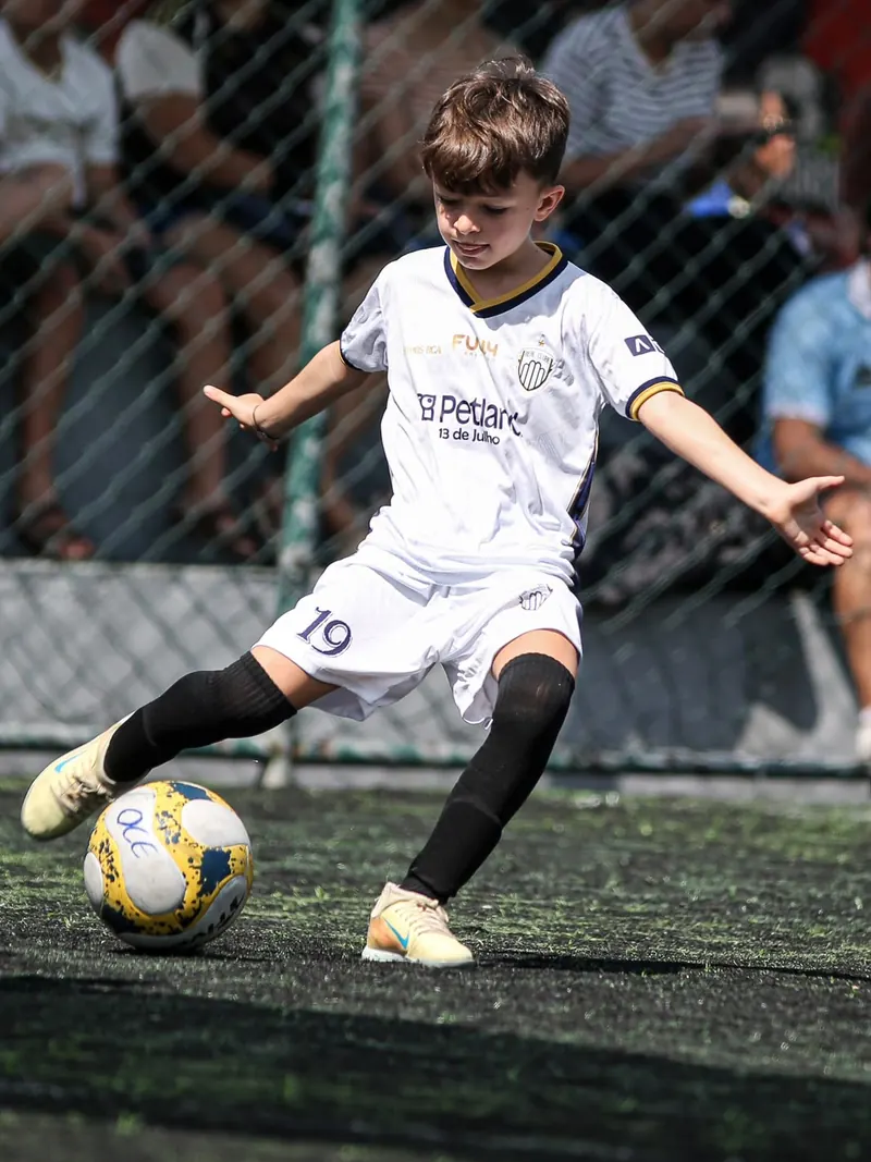 Atleta de uniforme branco prepara o chute, com a torcida atrás do alambrado