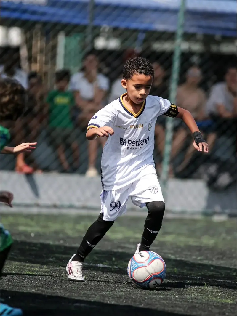 Atleta de uniforme branco conduz a bola durante o jogo